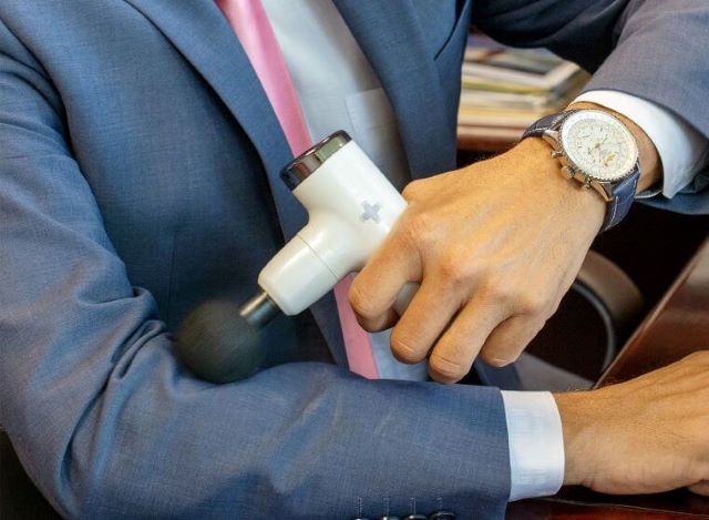 Person using a massage gun to self-massage forearm.