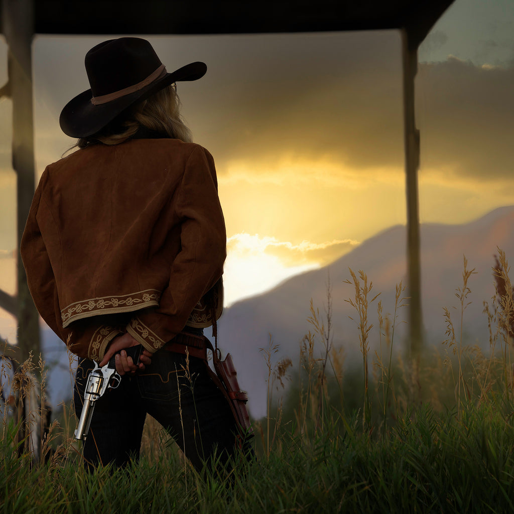 Bruce Dorn model wearing cowboy hat standing at sunset with six shooter gun behind back