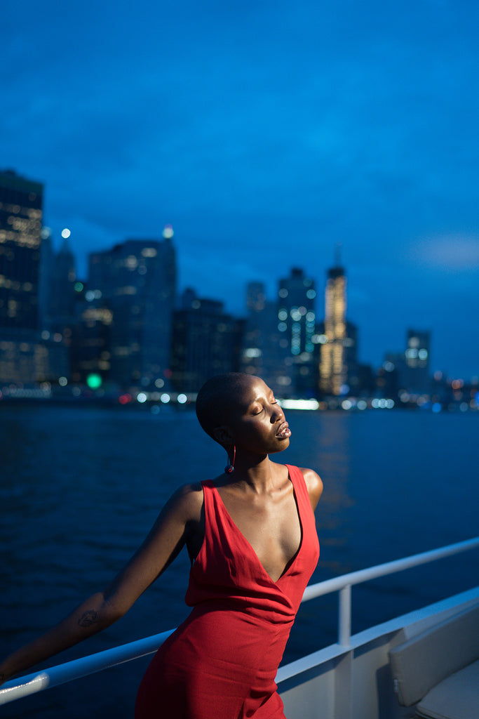 Sara France photograph of woman on boat wearing red dress cityscape in background 