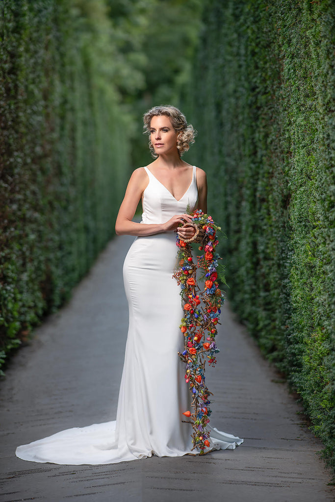 Yuliya Panchenko bride with bouquet standing in green hedgerow