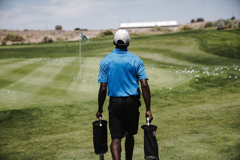 A man walking on the golf field with bags