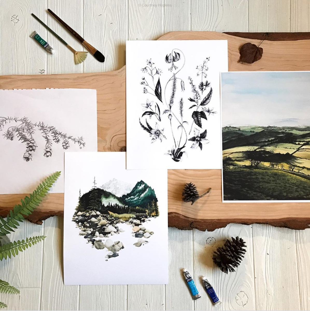 landscape and botanical art prints in a flatlay with wood and greenery