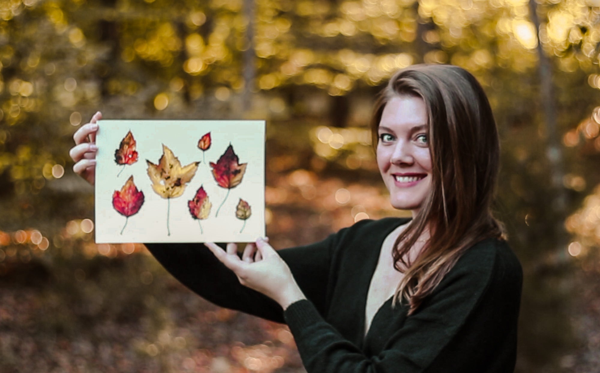 Courtney Hopkins holding up a painting of fall leaves