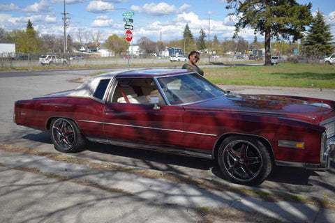 Delena smiling next to a full shot of the vintage maroon Cadillac.