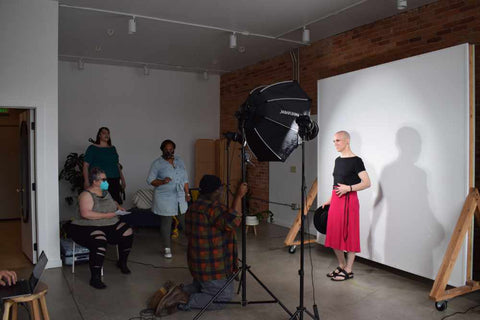 Wide shot of indoor photoshoot. Aubrey is being photographed while multiple models and staff observe.