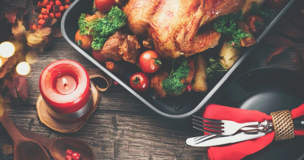 flatlay of festive turkey in a roasting tin with a red candle, napkin and cutlery