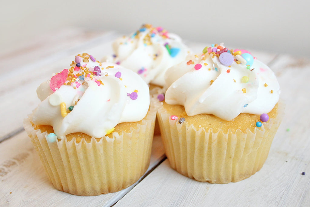 three sponge cupcakes decorated with white icing and covered in sprinkles and sugared treats