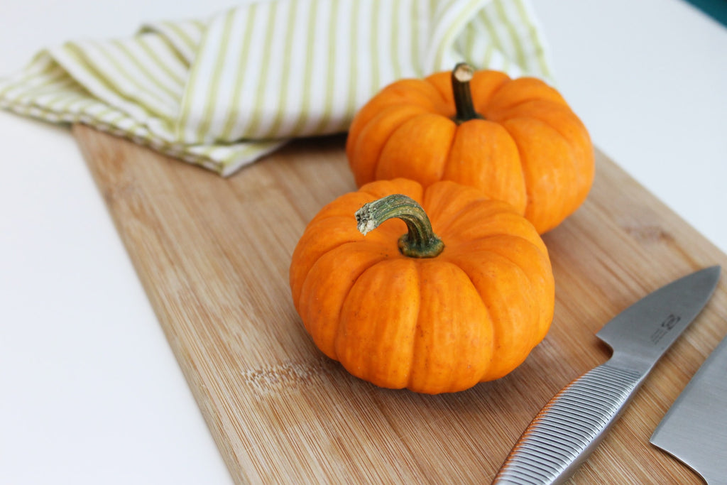 two mini pumpkins on a wooden chopping board next to a sharp knife