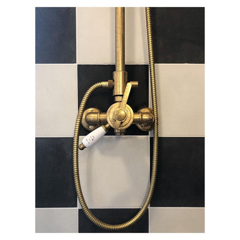 Unlaquered brass shower taps on black and white tiles