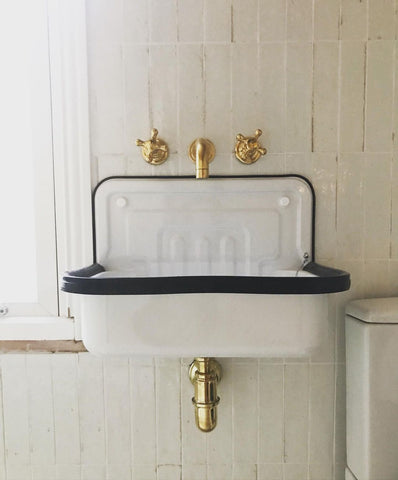 Wall mounted brass taps over enamel bathroom basin