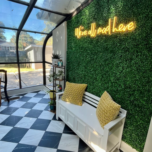 A yellow "we're all mad here" neon sign in a living room.