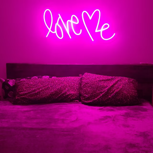 Love Me neon sign in deep pink above bed in bedroom