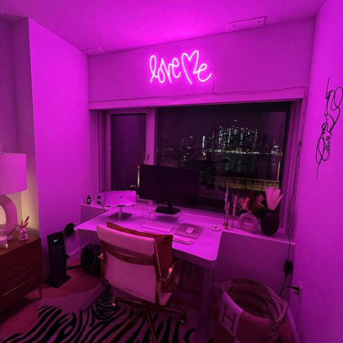 Love Me neon sign installed on wall above desk.