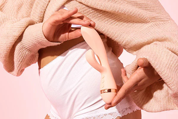Person wearing beige jumper and light pink intimate bottoms holding VUSH Muse Rabbit Vibrator against hip