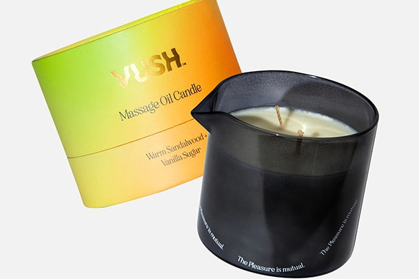 VUSH Massage Oil Candle orange/green/yellow gradient packaging cyclinder next to black glass candle