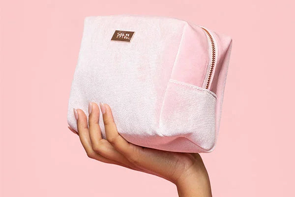 Hand holding light pink soft cosmetics bag with tag that reads 