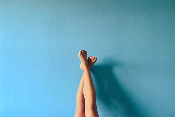 Legs up vertical with ankles crossed against a blue wall