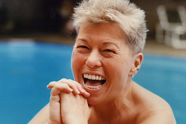 Betty with short grey hair laughing and smiling in front of swimming pool