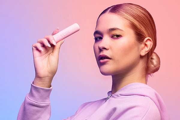 Young woman with blonde hair wearing purple hoodie holding VUSH Gloss small pink precision bullet vibrator