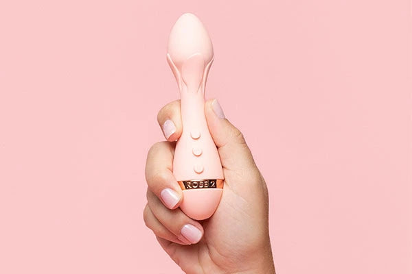 Hand holding light pink bullet vibrator against light pink background