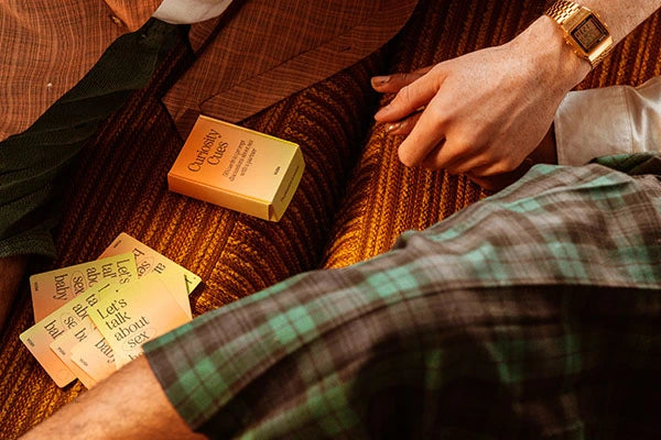 VUSH's Curiosity Cues displayed on orange velvet couch next to one hand and a checkered skirt