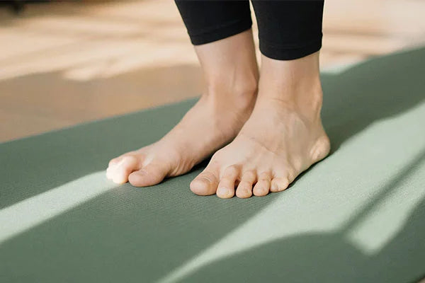 Person's ankles wearing black leggings and feet stepping on green pilates mat