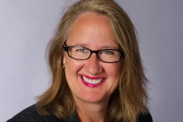 Helen smiling & wearing black glasses and pink lipstick against grey background