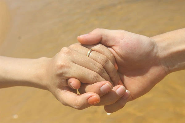 Two hands holding each other romantically on the shore of the beach