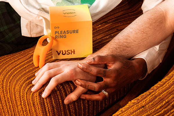 Couple holding hands on orange couch next to VUSH Orb pleasure ring and orange packaging