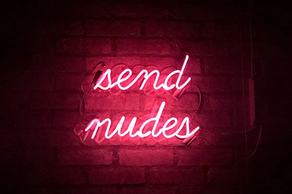 Pink neon sign that reads 'SEND NUDES' against brick wall