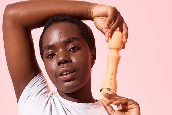 Person with shaved black hair holding Majesty 2 orange wand vibrator next to face