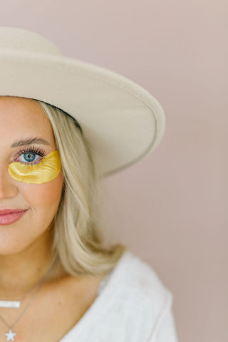 A woman wearing a hat and standing half in the frame with a gold lash lift shield under her eye.