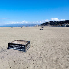 Large square fire pits scattered on the sand along a beach 