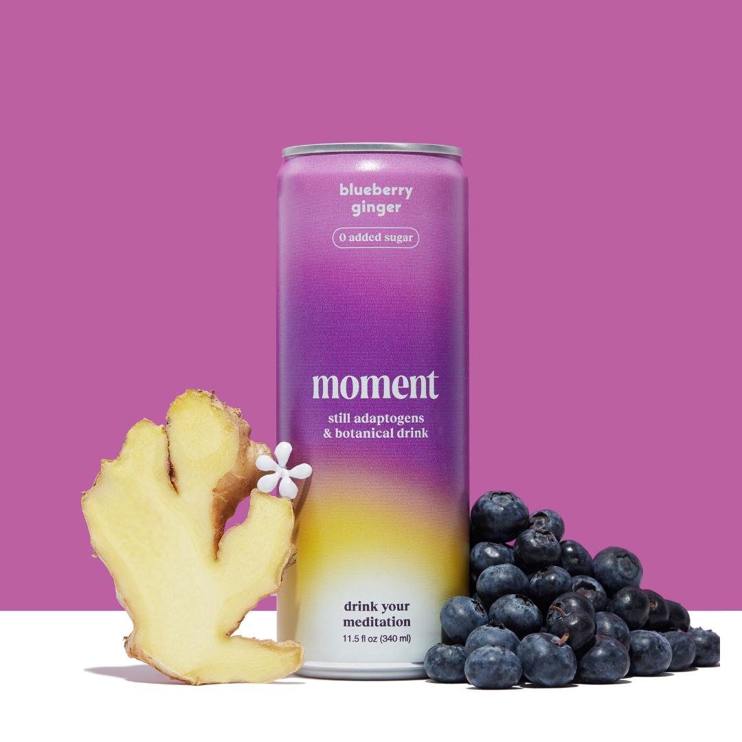 A can of Moment blueberry ginger drink with fresh ginger and blueberries on a purple background.