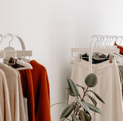 close up of neutral color clothing on a white metal free standing clothing rack with a plant in front