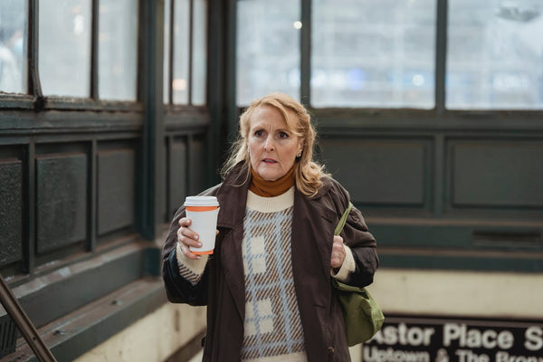 elderly woman holding a cup of coffee and a green tote bag