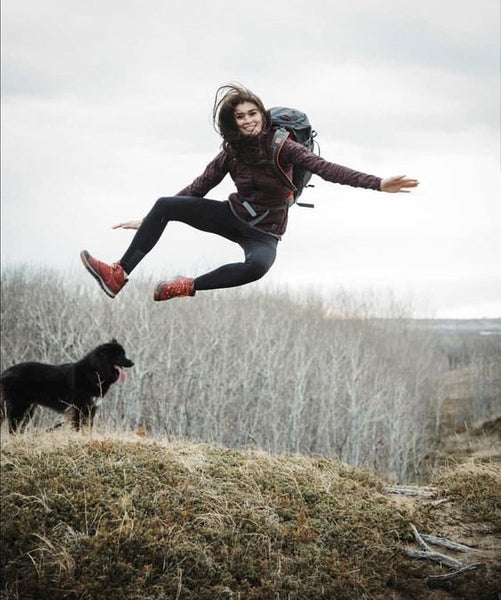 girl jumping in a field above a black dog