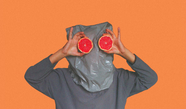 man with gray plastic bag on head holding red oranges for eyes