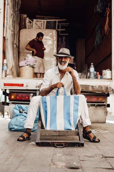 man with white beard holding a tote bag with blue and white stripes