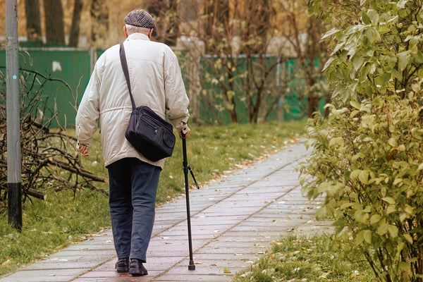 Elderly person walking on path with cane in right hand