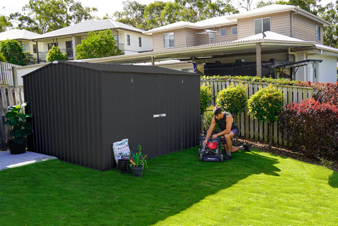 A man with lawnmower beside the Absco Premier 10 feet Metal Outdoor Storage Monument Shed.