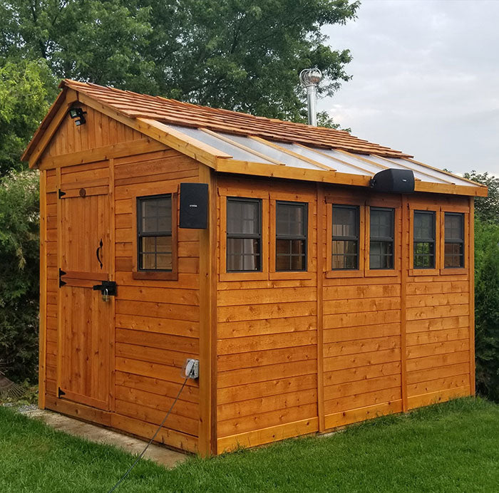 Fully-equipped Outdoor Living Today Sunshed Garden Shed, 8x12, featuring a wooden exterior with functional windows and exterior lighting, surrounded by greenery.