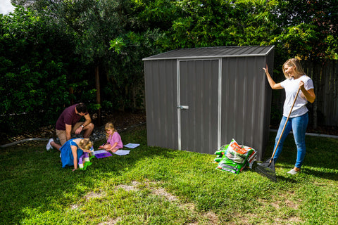 The Absco Space Saver Metal Garden Shed 7.5' x 5' with a family in a backyard setting.