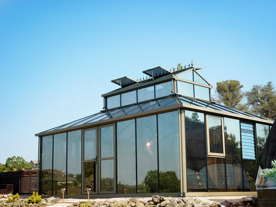 A stunning glass greenhouse with a roof, perched atop a hill. Exaco Janssens Cathedral Victorian Greenhouse with Large Cupola, 15 x 20 ft.