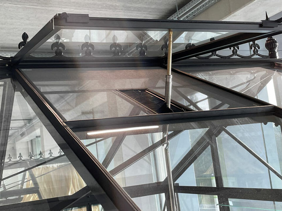 A detailed view of a Janssens Greenhouse showcasing the automatic roof vent in an open position, and the fly screen protecting the interior.