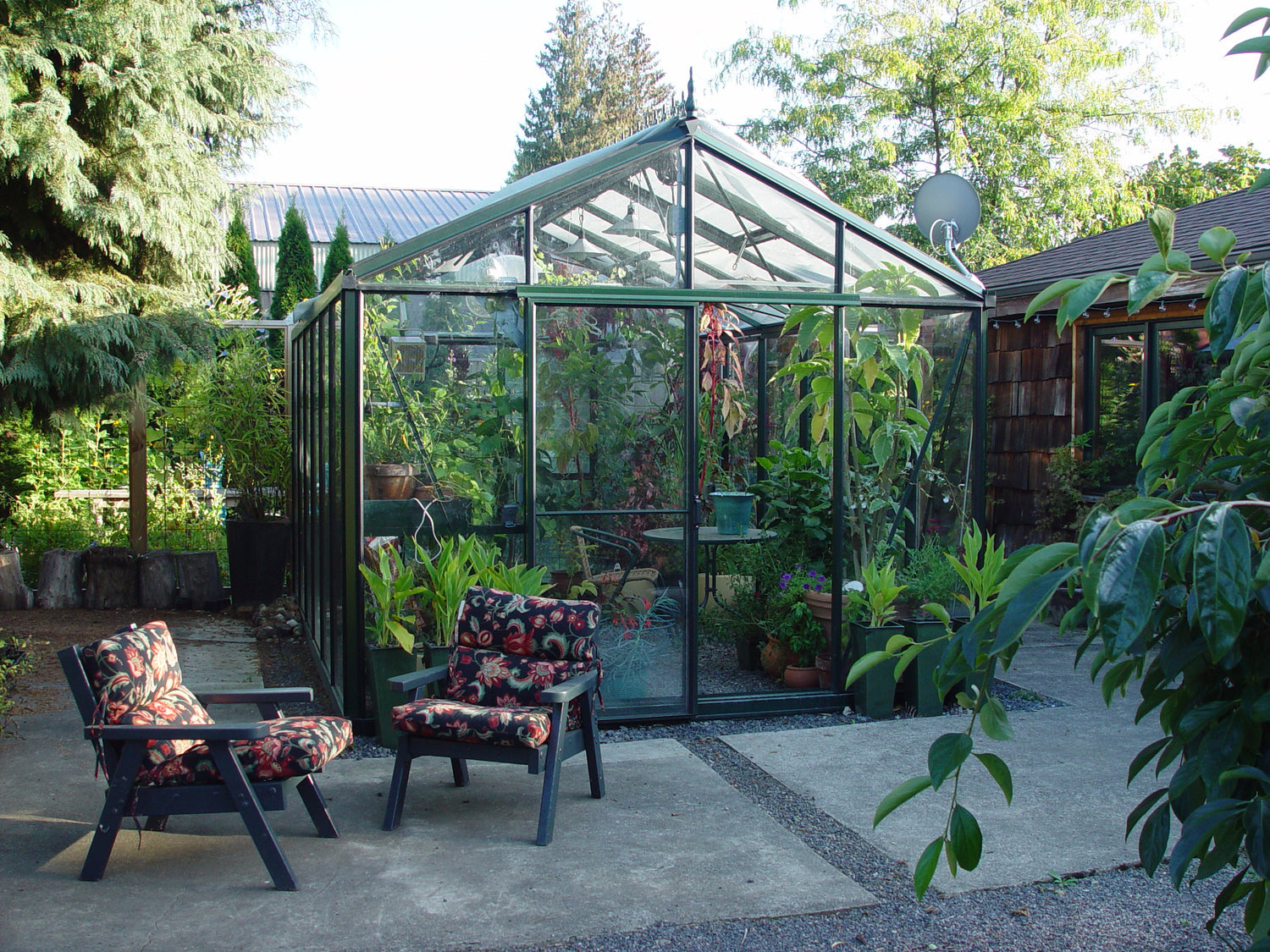 Ornate Janssens Victorian Royal VI-34 greenhouse with black framing and glass panes surrounded by a garden.