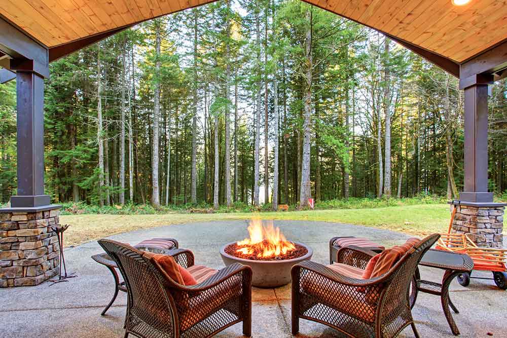 Spacious outdoor patio with a fire pit and wicker chairs, overlooking a lush forest
