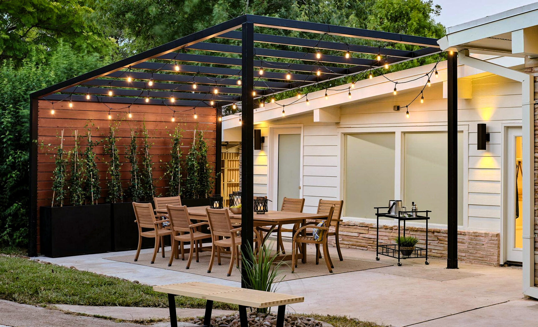 black pergola with outdoor string lights and dining set on pavement