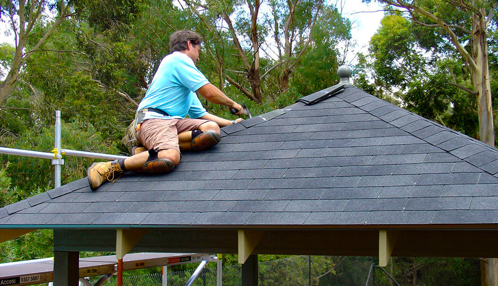 man attaching shingles on gazebo roof using a hammer