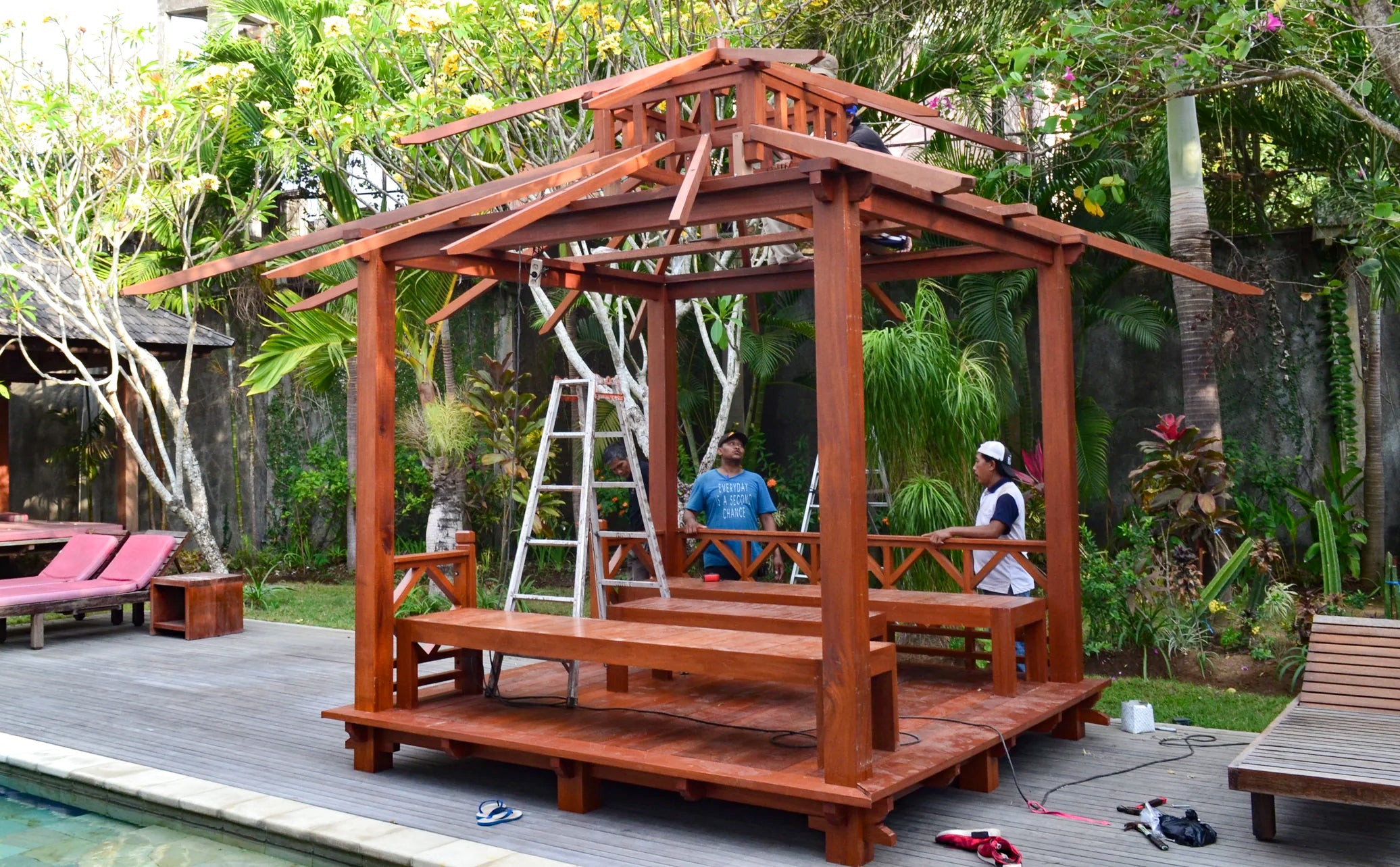 men assembling the exaco bali gazebo beside a pool